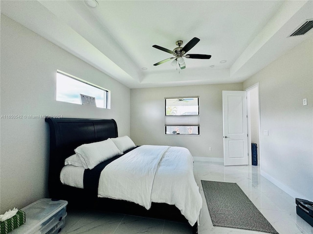 bedroom with a raised ceiling, multiple windows, and ceiling fan