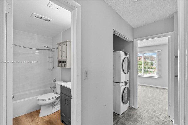 full bathroom with tiled shower / bath, hardwood / wood-style flooring, toilet, stacked washer and dryer, and vanity