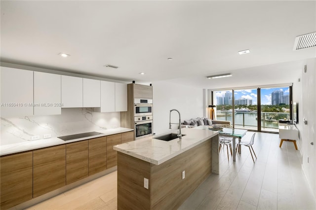 kitchen with white cabinetry, an island with sink, sink, double oven, and black electric cooktop