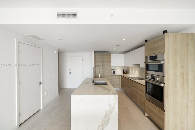 kitchen with sink, light stone countertops, light wood-type flooring, and decorative backsplash