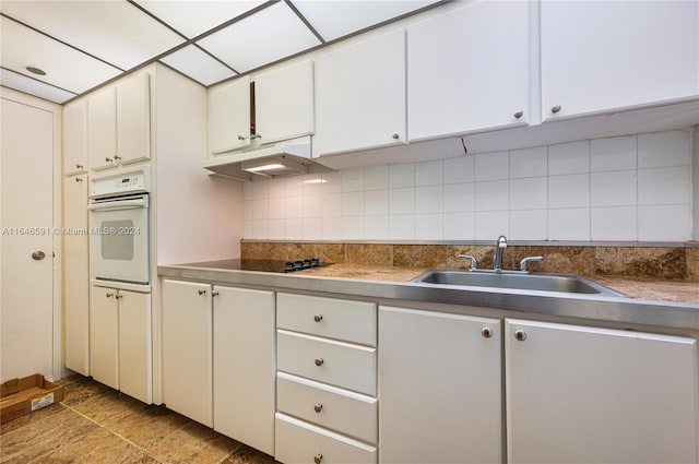 kitchen with white oven, white cabinetry, backsplash, light tile patterned floors, and sink