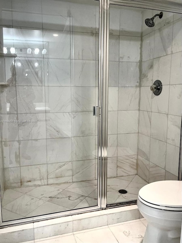 bathroom featuring a shower with door and toilet