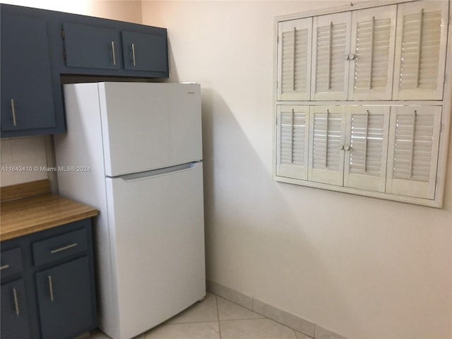 kitchen with light tile patterned floors, blue cabinetry, and white refrigerator