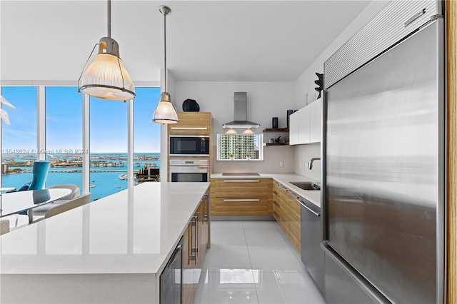 kitchen featuring hanging light fixtures, a center island, sink, wall chimney exhaust hood, and built in appliances