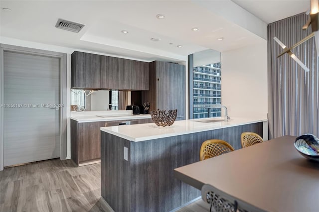 kitchen featuring sink, kitchen peninsula, light hardwood / wood-style floors, a kitchen bar, and dark brown cabinets