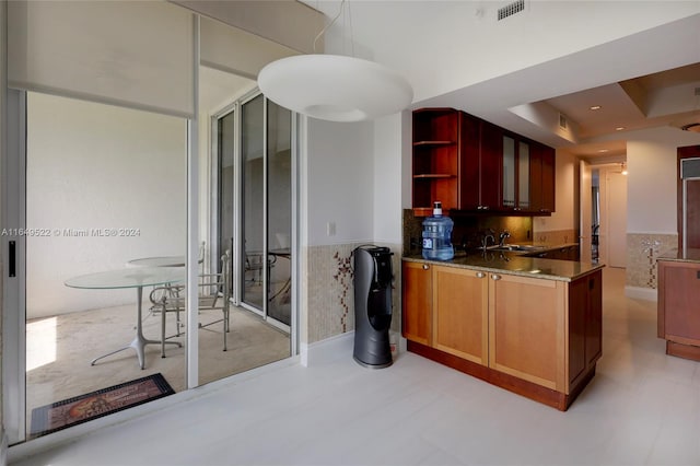 kitchen featuring a tray ceiling, dark stone counters, sink, and hanging light fixtures