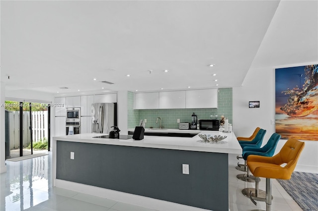 kitchen with backsplash, light tile patterned floors, black appliances, a breakfast bar area, and white cabinets