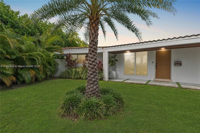 back of house at dusk with a yard and stucco siding