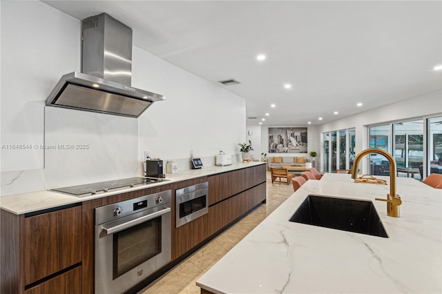 kitchen featuring visible vents, modern cabinets, appliances with stainless steel finishes, wall chimney range hood, and a sink