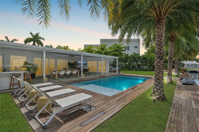 pool with a deck, a yard, and ceiling fan