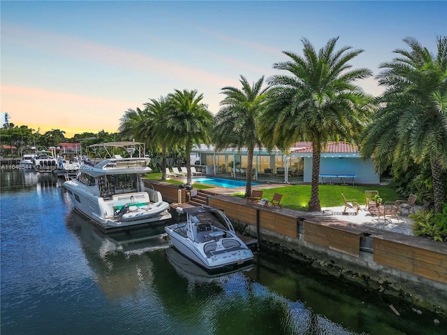 view of dock with a water view, a patio area, a community pool, and a yard