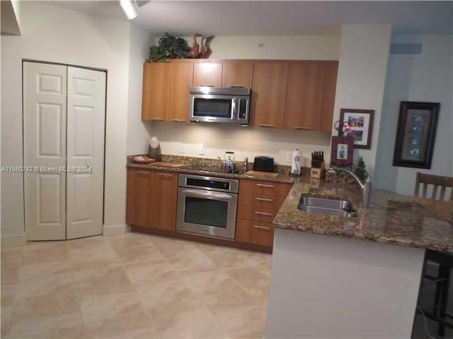 kitchen featuring appliances with stainless steel finishes, dark stone countertops, kitchen peninsula, and sink