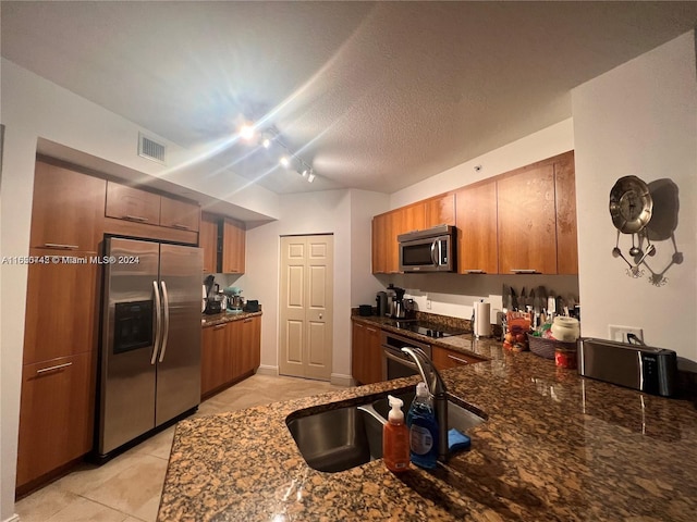 kitchen with a textured ceiling, rail lighting, light tile patterned floors, stainless steel appliances, and sink