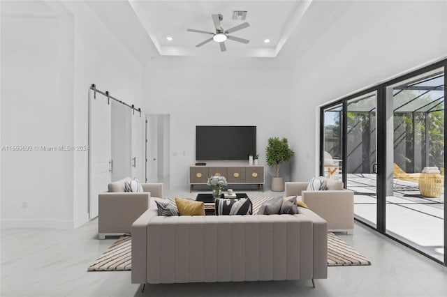 living room featuring a raised ceiling, a high ceiling, ceiling fan, and a barn door