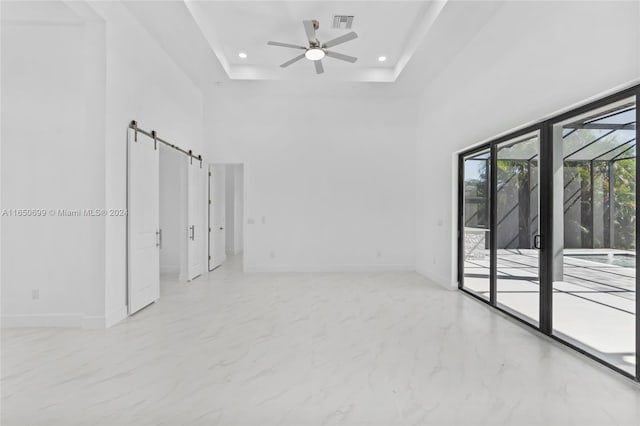 unfurnished room with a barn door, ceiling fan, a raised ceiling, and a high ceiling