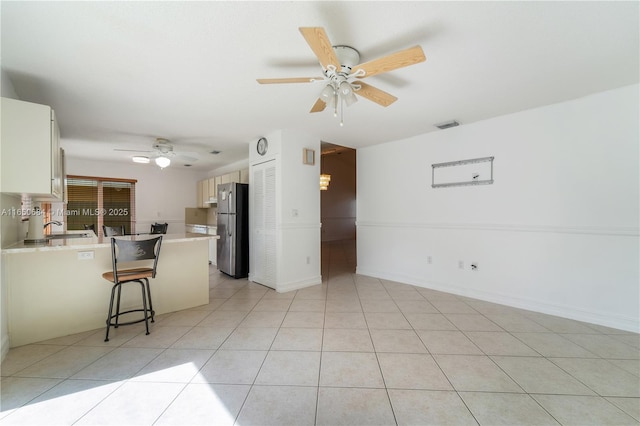 kitchen featuring a breakfast bar, light tile patterned floors, light countertops, freestanding refrigerator, and a sink