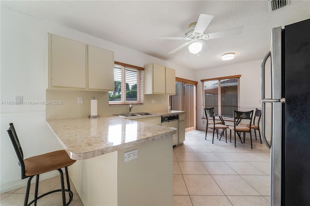 kitchen featuring light countertops, cream cabinets, freestanding refrigerator, a peninsula, and a kitchen breakfast bar