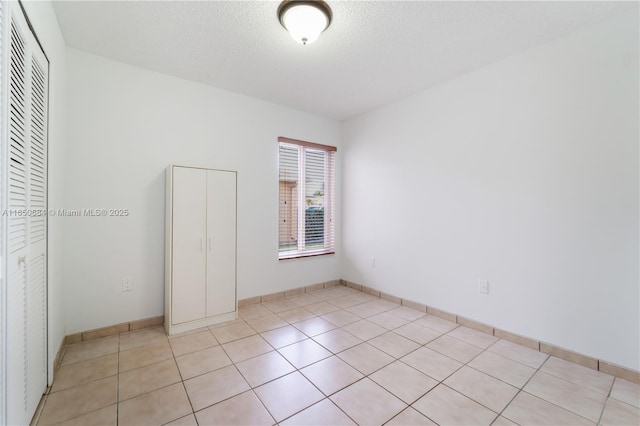 spare room with light tile patterned floors, baseboards, and a textured ceiling