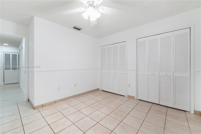 unfurnished bedroom featuring light tile patterned floors, multiple closets, visible vents, a ceiling fan, and baseboards