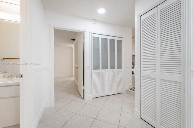 hall featuring a sink, a textured ceiling, and light tile patterned flooring