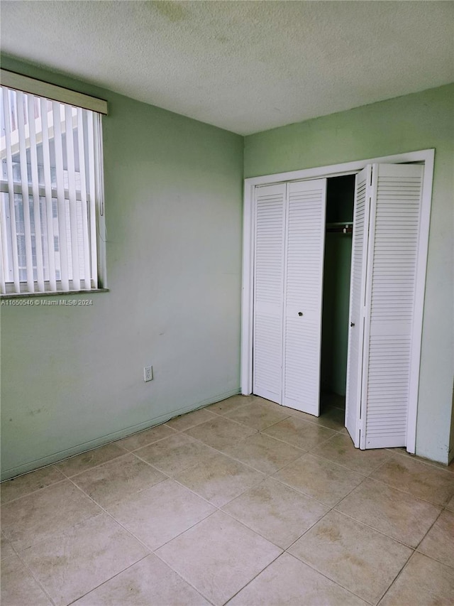 unfurnished bedroom featuring a textured ceiling, light tile patterned floors, and a closet