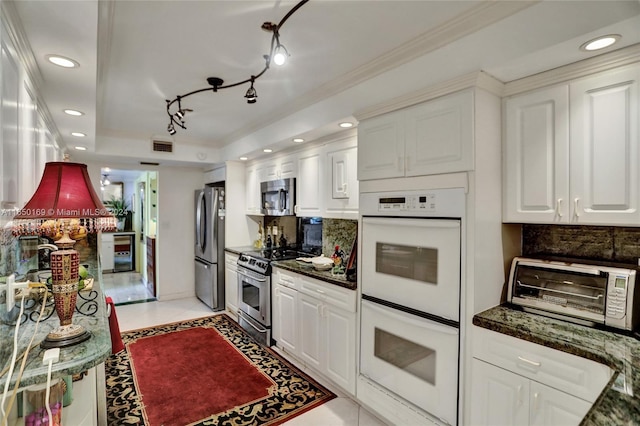 kitchen featuring white cabinets, appliances with stainless steel finishes, dark stone countertops, and decorative backsplash