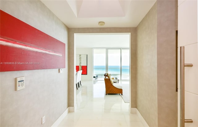 corridor with a wall of windows, a tray ceiling, and light tile patterned flooring