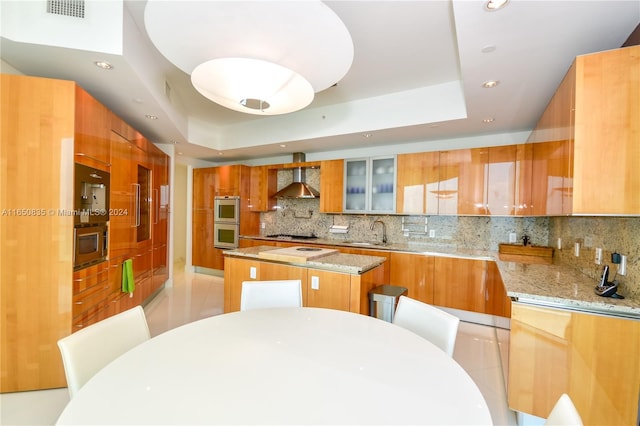 kitchen featuring light stone counters, a kitchen island, decorative backsplash, and wall chimney range hood