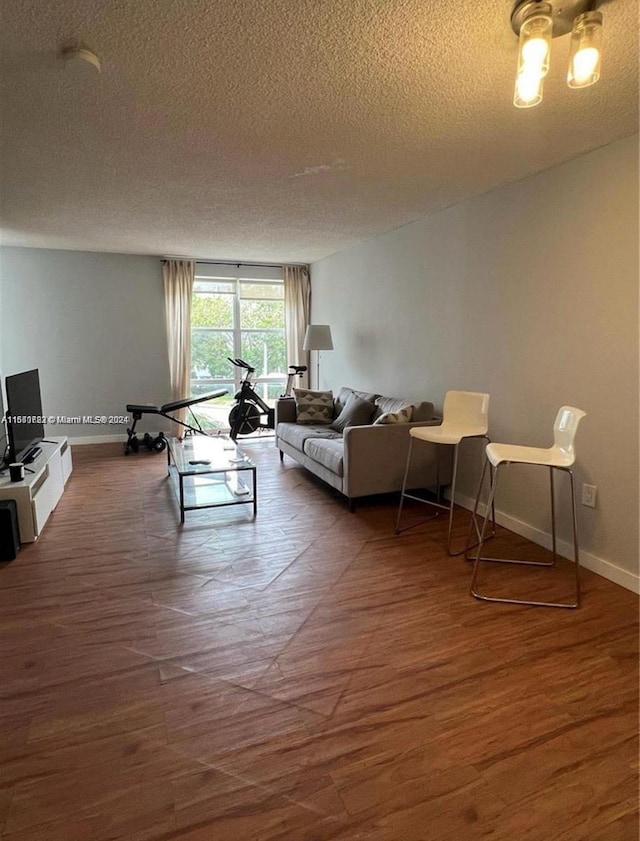 living room with a textured ceiling, baseboards, and wood finished floors