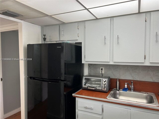 kitchen with black fridge, white cabinets, decorative backsplash, and sink