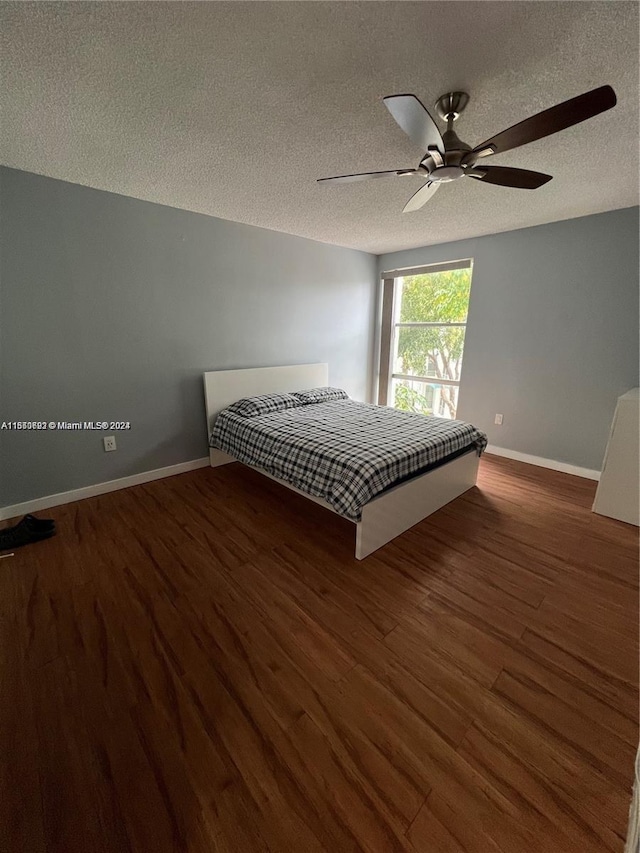 unfurnished bedroom featuring a ceiling fan, a textured ceiling, baseboards, and wood finished floors