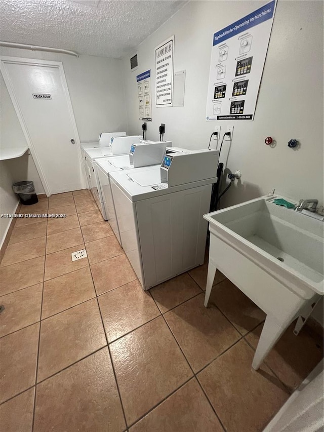 common laundry area with washer and clothes dryer, a textured ceiling, and light tile patterned flooring