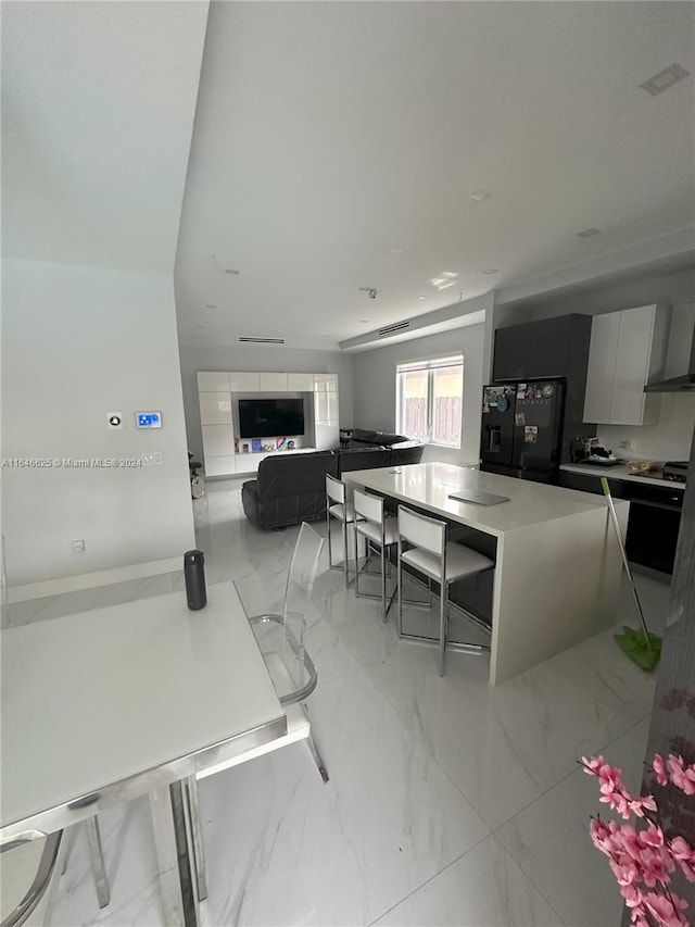 kitchen with black refrigerator with ice dispenser, a large island, and white cabinetry