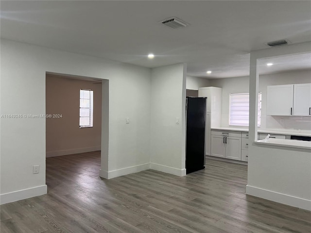 kitchen with white cabinetry, black refrigerator, hardwood / wood-style flooring, and tasteful backsplash