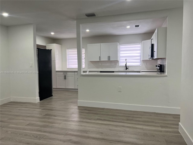 kitchen with black refrigerator, white cabinets, plenty of natural light, and light hardwood / wood-style floors