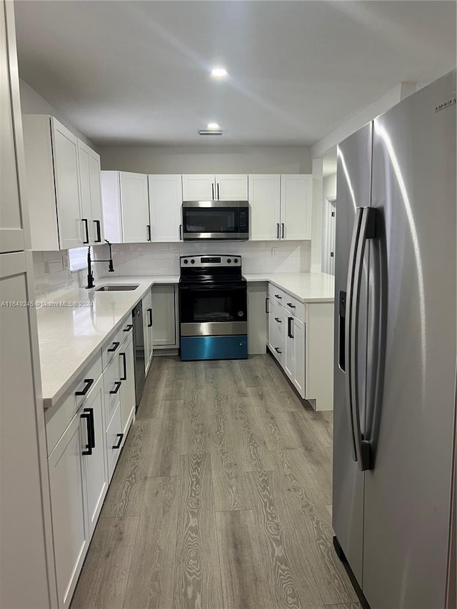 kitchen with stainless steel appliances, sink, white cabinetry, and light hardwood / wood-style flooring