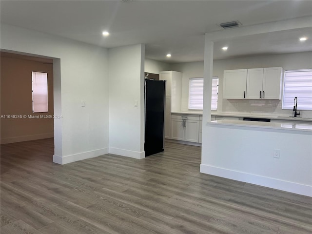 kitchen with white cabinets, sink, backsplash, light wood-type flooring, and black refrigerator