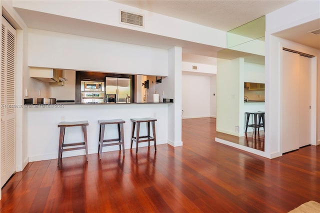 kitchen with a breakfast bar, appliances with stainless steel finishes, dark hardwood / wood-style flooring, and kitchen peninsula