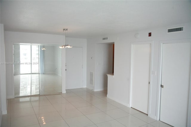 tiled spare room with a notable chandelier