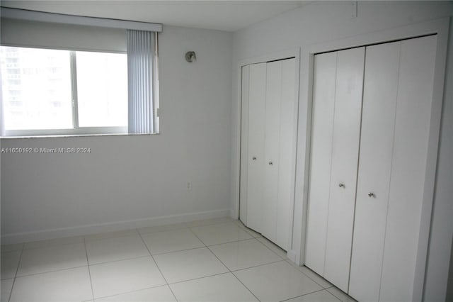 unfurnished bedroom with light tile patterned floors and multiple closets