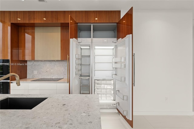 kitchen featuring black electric stovetop, light stone countertops, tasteful backsplash, and sink