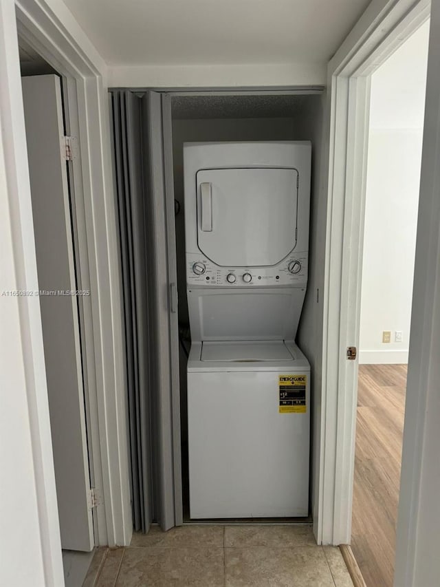 laundry room featuring stacked washing maching and dryer and light tile patterned floors