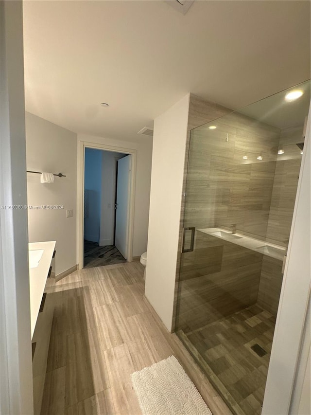 bathroom featuring a shower with shower door, toilet, wood-type flooring, and vanity