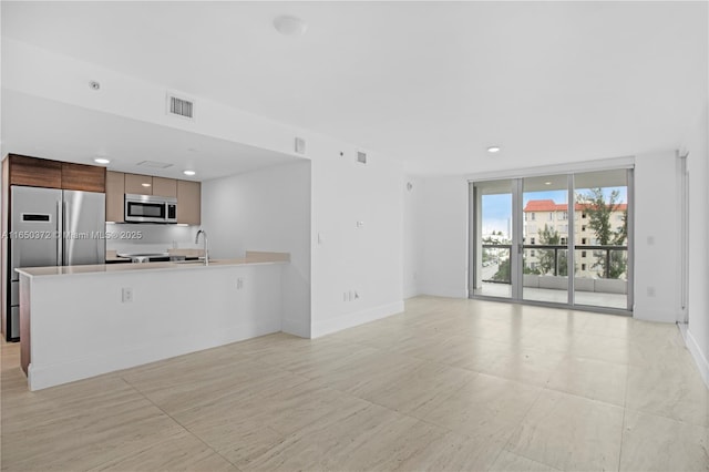 unfurnished living room featuring baseboards, floor to ceiling windows, visible vents, and a sink