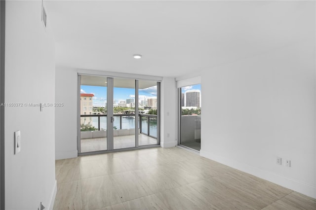 spare room with visible vents, baseboards, a water view, expansive windows, and a city view