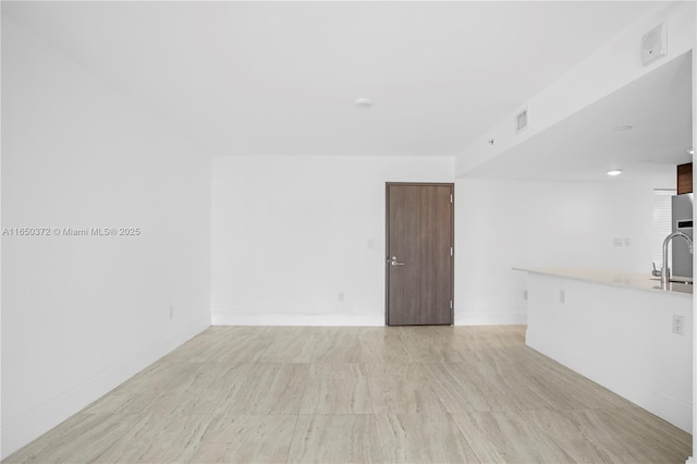 unfurnished living room with a sink, visible vents, and baseboards