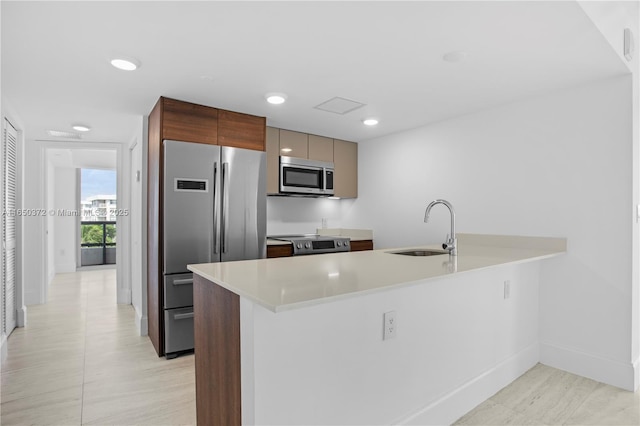 kitchen featuring recessed lighting, stainless steel appliances, a peninsula, a sink, and light countertops