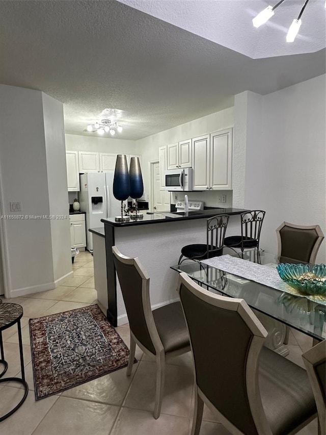 kitchen with white appliances, white cabinetry, kitchen peninsula, a kitchen bar, and a textured ceiling