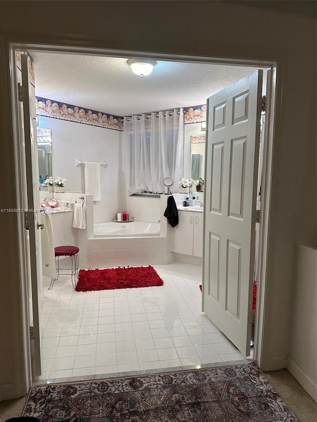 bathroom featuring tile patterned flooring, a textured ceiling, tiled bath, and vanity