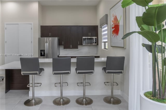 kitchen featuring stainless steel appliances, a kitchen breakfast bar, light tile patterned floors, and dark brown cabinets